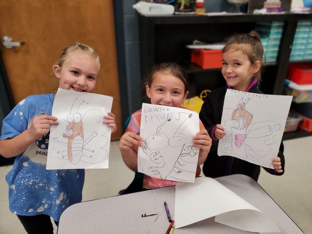 3 girls holding up drawings