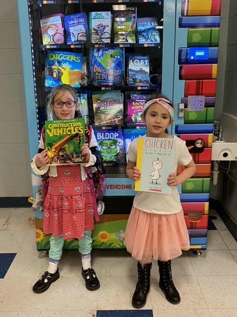 girls holding books in front of vending machine