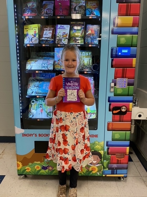 student holding book in front of vending machine